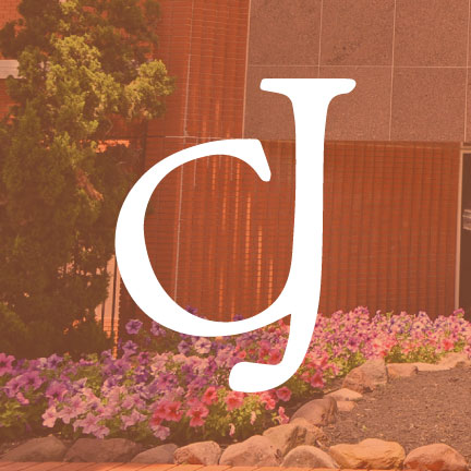 Image: Front of red brick building with a large sundial and flower garden, overlaid with an orange transparency and the letters CJ.